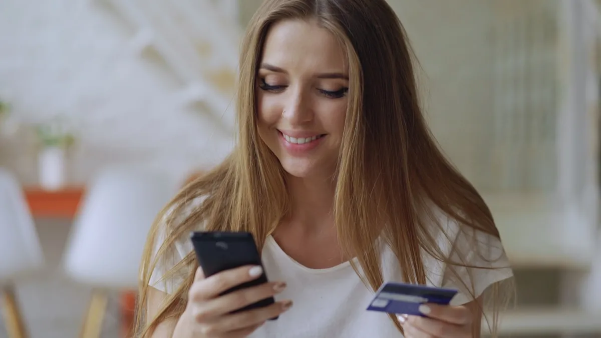 Woman checking her phone while holding a credit card, representing the online gold purchasing process