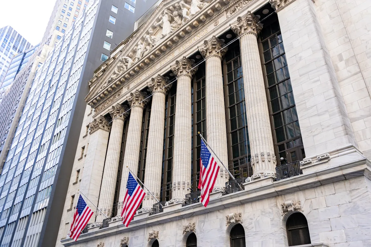 NYSE building with American flags representing the financial markets that influence gold pricing