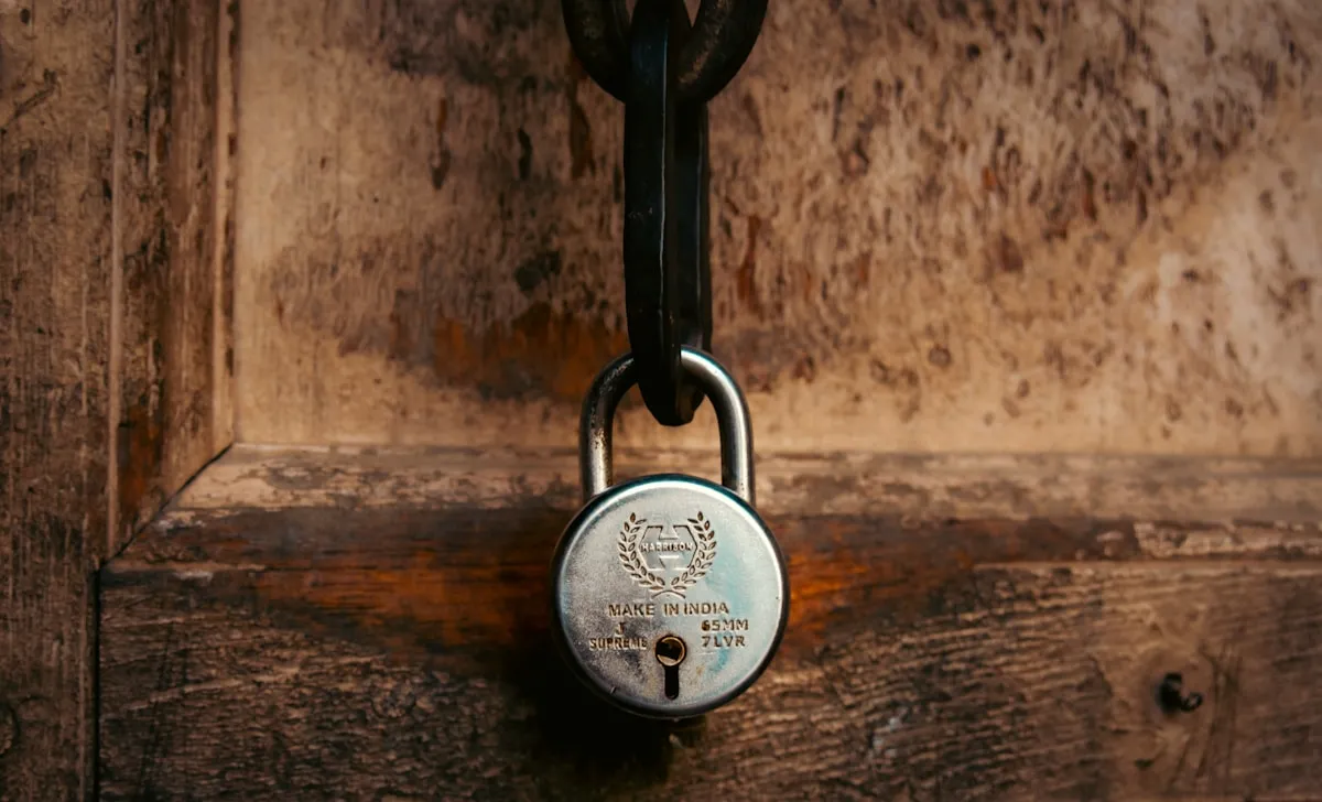 A padlock secures an old wooden door, illustrating that even behind locked doors, environmental enemies like humidity and temperature silently attack unprotected metals